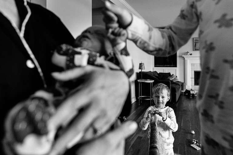 boy holds small camera while older boy holds newborn hands, framing the center boy for photos in at home