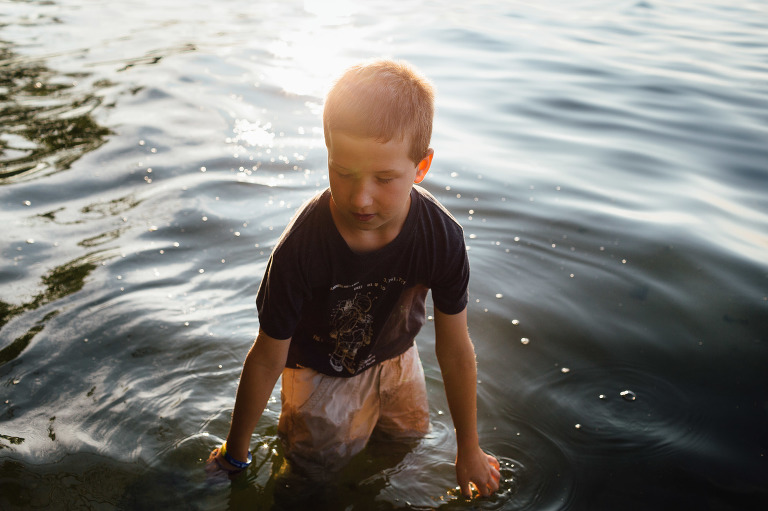Boy wades in shallow lake water near sunset.