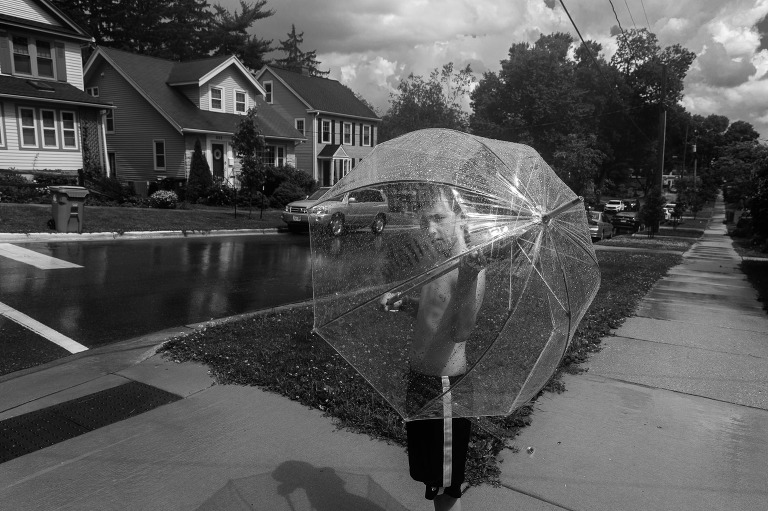 Boy stands on sidewalk in a rain and sunshine storm. Interesting light and shadows. 