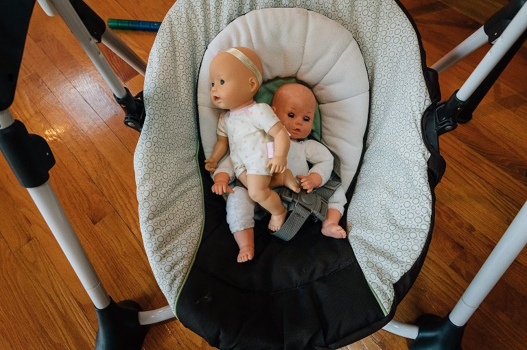 Two dolls sit in the seat of a baby swing. 