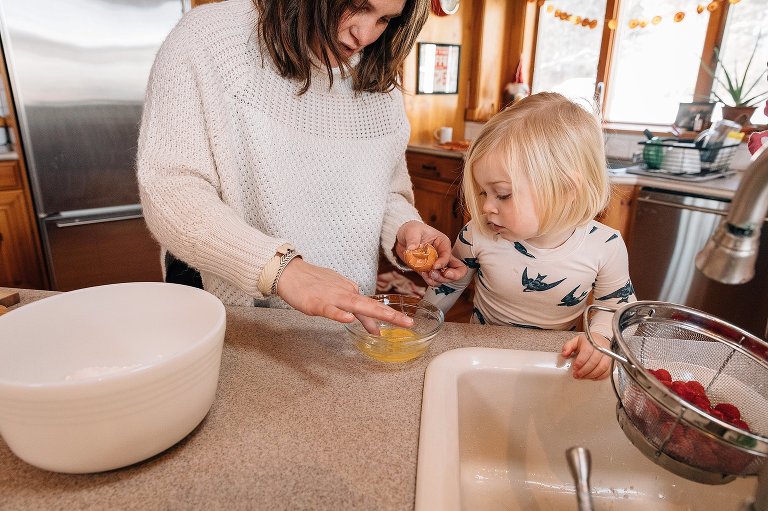 Mom and toddler daughter pluck an eggshell out of a cracked egg in a bowl. 