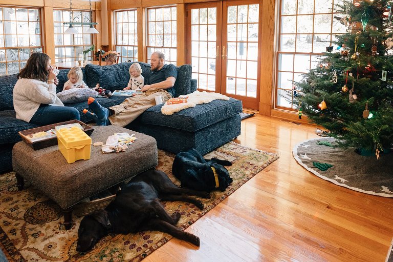 Family of five and two dogs relax in the living room. Christmas tree in the corner. 