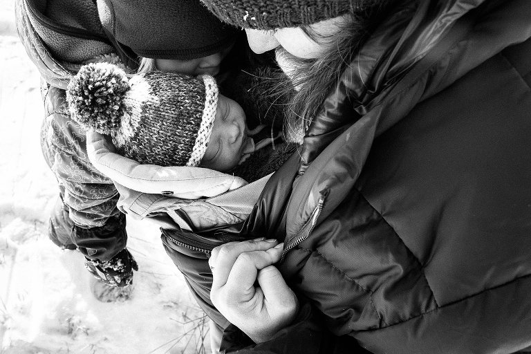 Mom has newborn snuggled into her winter jacket. 
