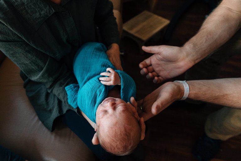 Set of hands reach for newborn in window light.