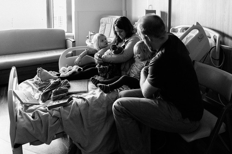 black and white. Family of 5 sits on a hospital bed after newborn arrives