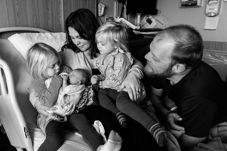 Black and white. Family of 5 cuddle on the hospital bed 