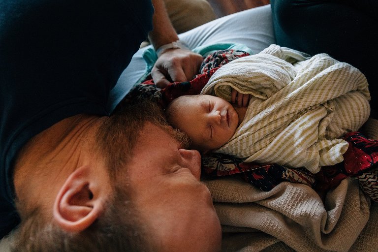 Dad lies face to face with newborn child on a hospital bed after birth
