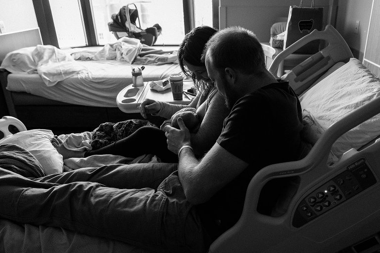 Black and white. Two parents squeeze onto same hospital bed after new baby was born. newborn photo