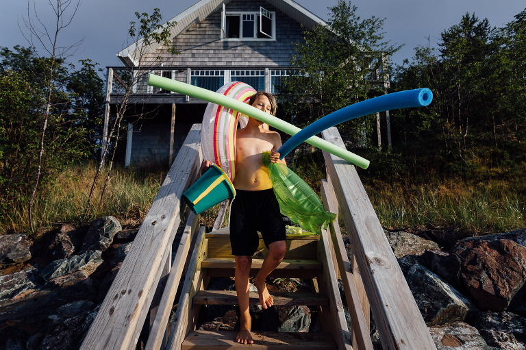 Boy carries all the beach supplies in his arms as he goes to the beach. 