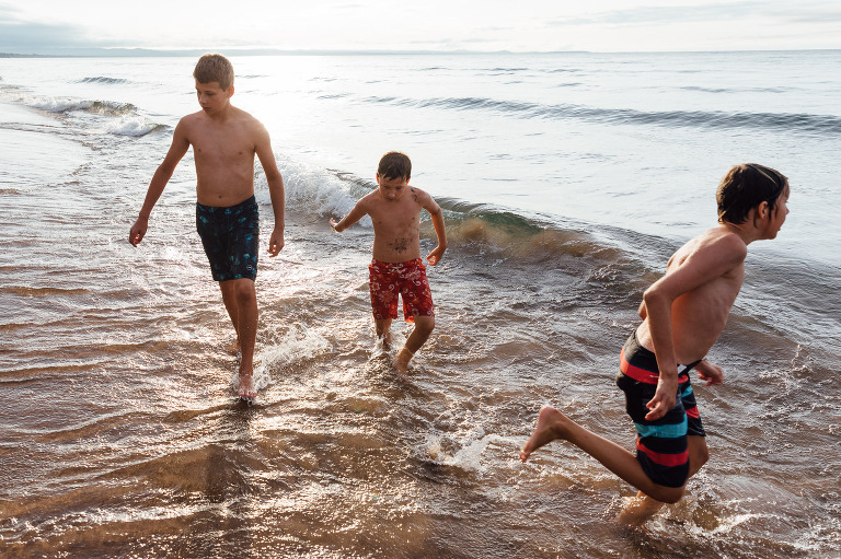 Three boys run at the beach. 