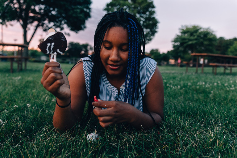 Girl eats Dilly Bar in a field at sunset. 