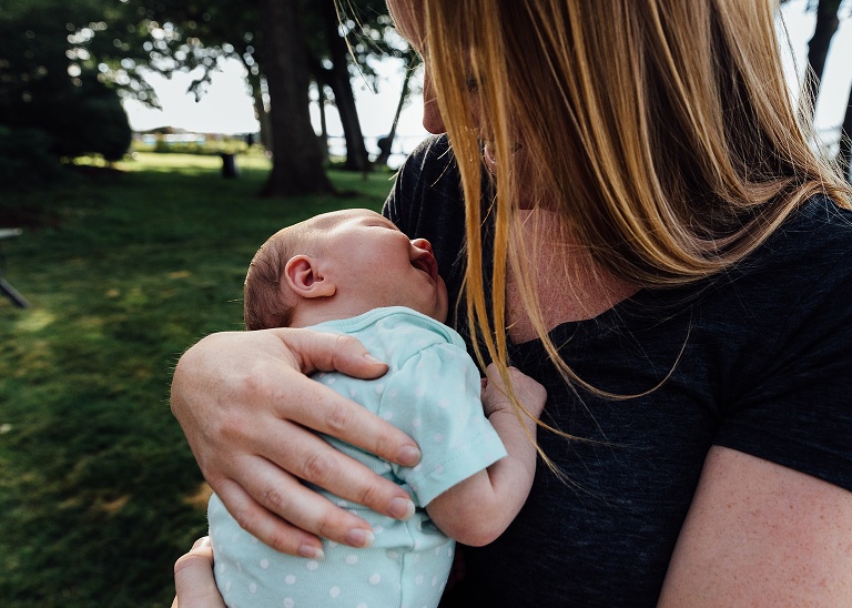 New mothers holds newborn outside, baby smiles. 