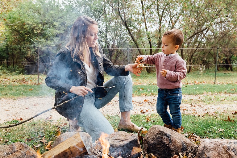Mothers helps preschool son make a s'more over a fire pit.