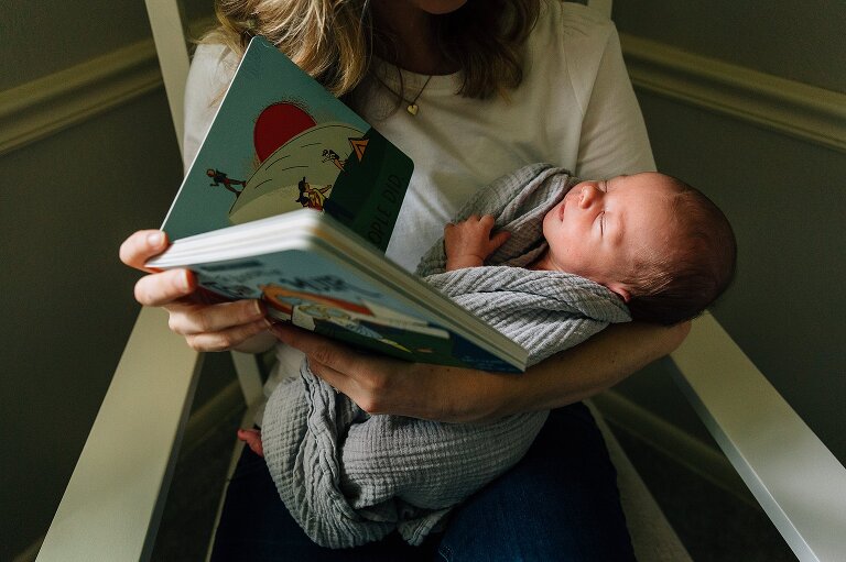 Baby held while mother reads a book. Newborn photography at home.