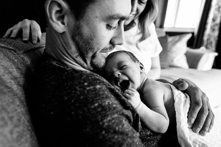 black and white. Baby yawns while Dad looks down at him. 