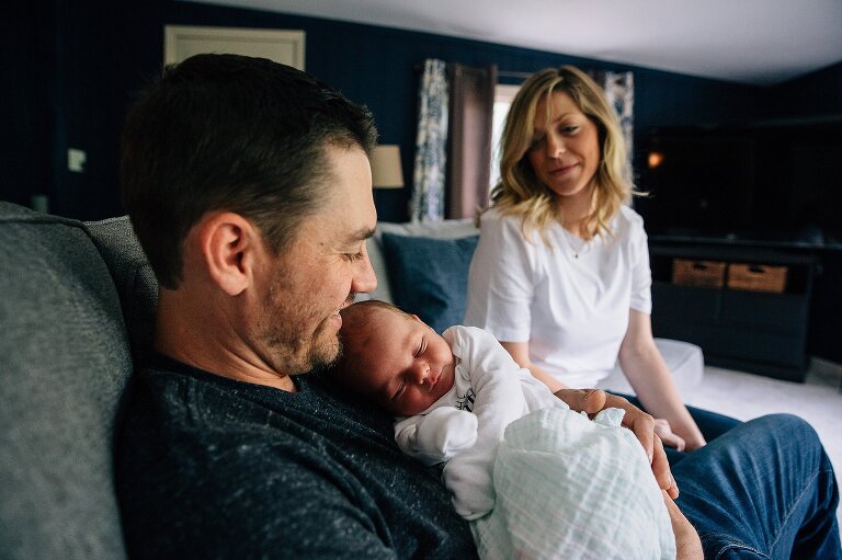 Dad holds newborn while mom smiles and looks on during an at-home photography session