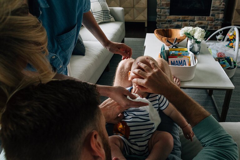 Mom cleans under baby's neck while dad holds baby's neck folds