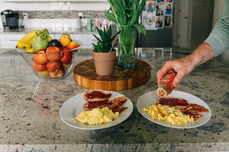 Man sprinkles spice on prepared scrambled eggs 