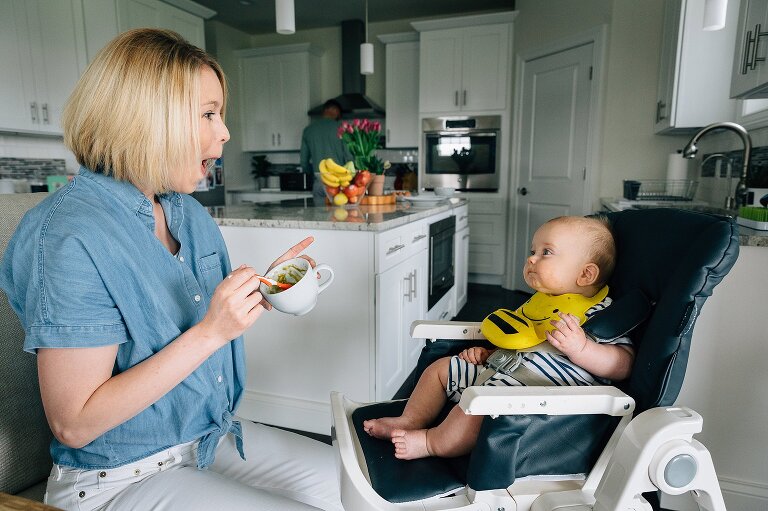 Mom opens her mouth while baby closes his with spoonful of mashed bananas