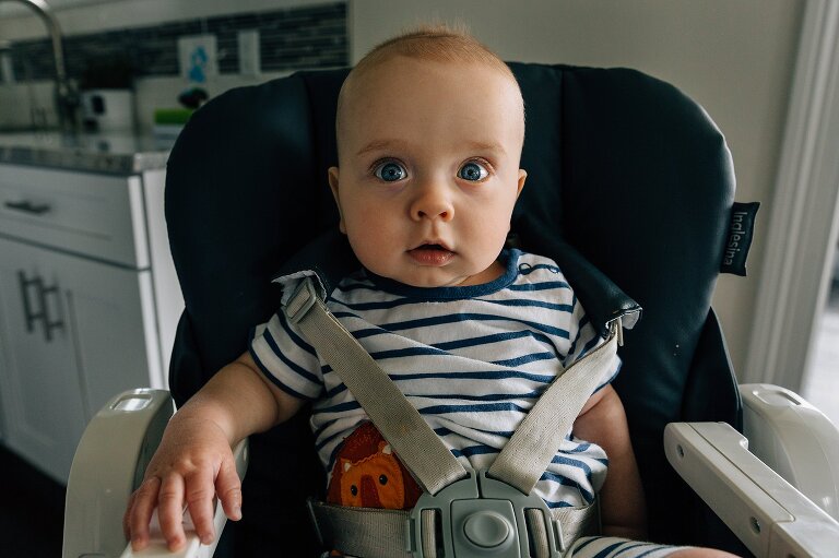 Baby sits in a high chair with big blue eyes and small smile