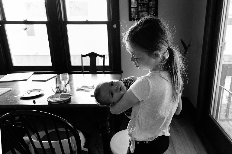 Big sister holds infant in her arms on. an ordinary summer Saturday morning