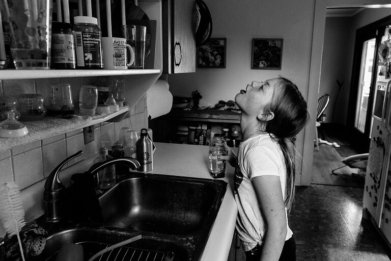 Black and white. Girl gargles water at the kitchen sink on an ordinary summer Saturday morning.