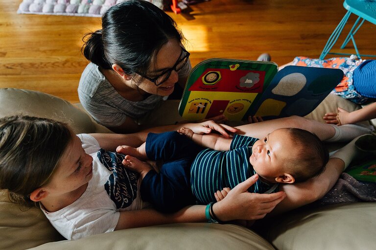 Big sister holds infant while Mom reads a story to both of them