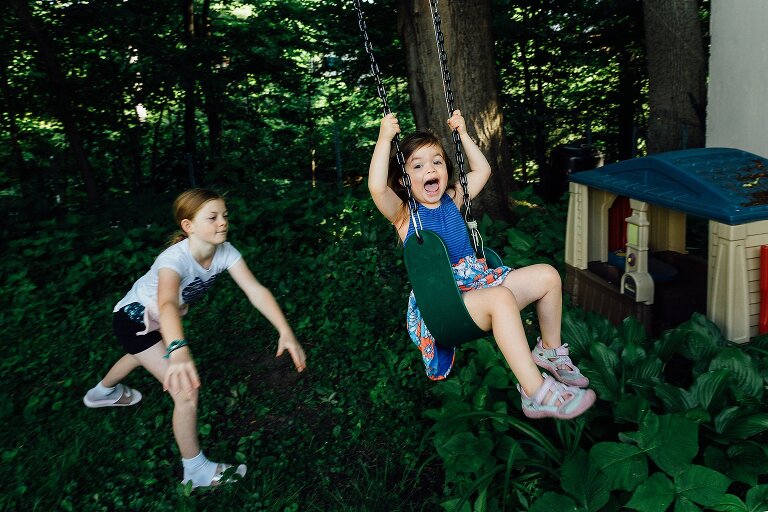 Preschool girl shouts with joy as older sister pushes her on a swing in the backyard