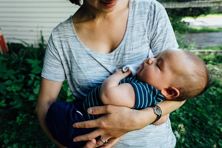 Mom holds sleeping infant in her arms in the backyard on an ordinary summer Saturday morning