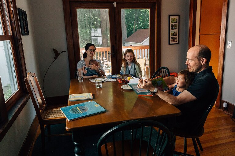 Family of five sits at the table eating breakfast and reading books on an ordinary summer Saturday morning
