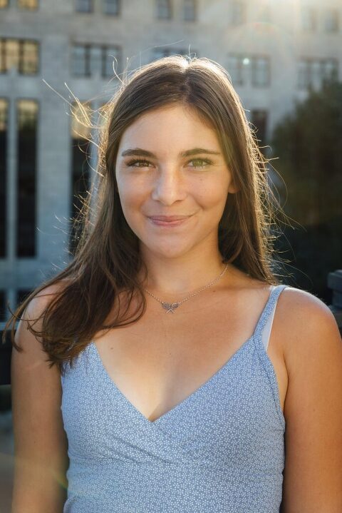 picture of high school senior girl smiling with city buildings and sunflare in the background