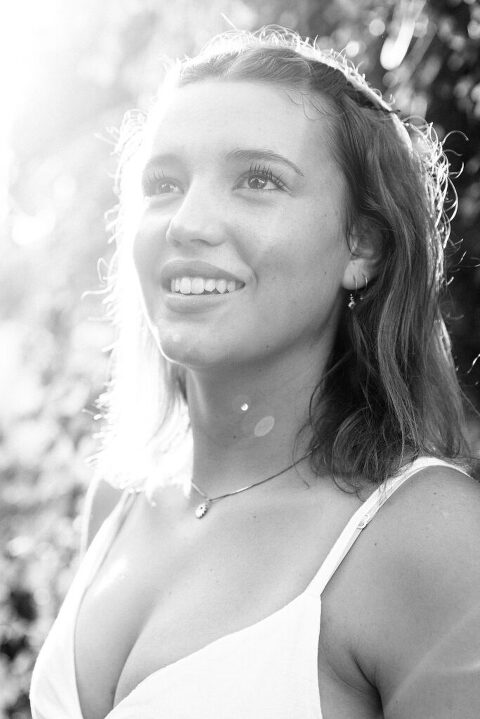 black and white. High school senior portrait. Girl looking off camera with sun flare across her face