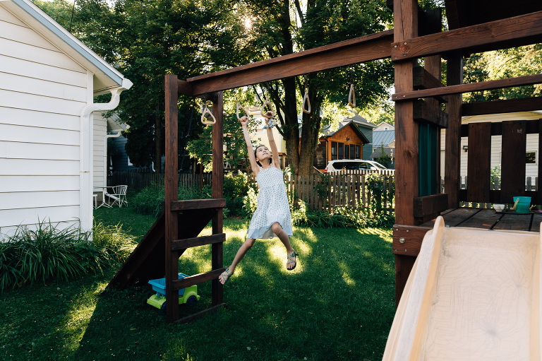 Girl swings on backyard monkey bars in beautiful summer light