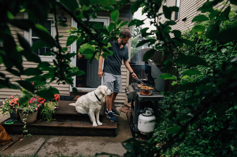 Man grills vegetables while dog watches.
