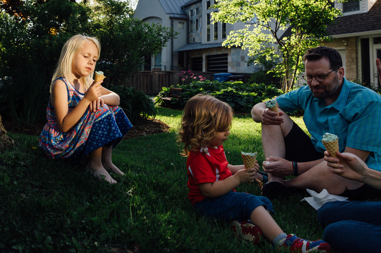 Family eats ice cream in the front yard of their home. 