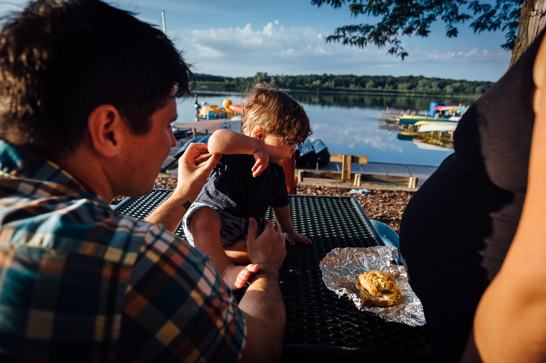 Family eats breakfast at a picnic table at the lake. Maternity photos. Outside Family Photography Activity Ideas