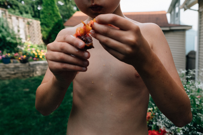 Boy eats peach in the backyard. Juice drips all over hands.