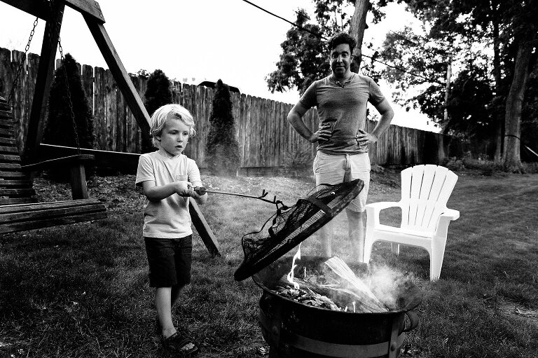 Boy removes protective cover of backyard campfire and reveals smoke. 