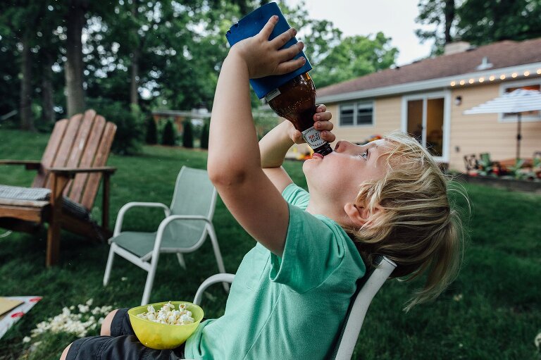 Boy drinks root beer from a bottle in front of a backyard campfire.