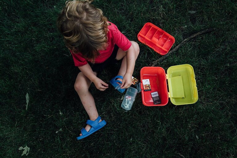 Boy empties tackle box on the grass. Very colorful scene. 