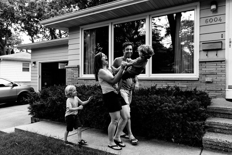 Black and white. Family of four playfully walk and smile as mom holds young son.
