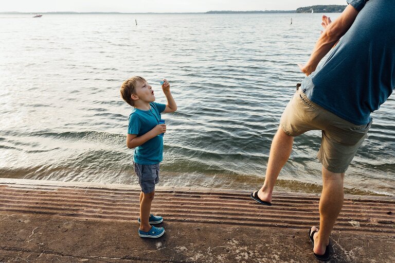At the beach, Boy blows bubbles at dad who dramatically reacts to a bubble attack. 
