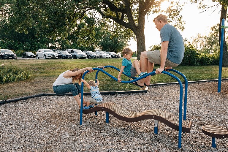 Family of four play on playground equipment at the park. 