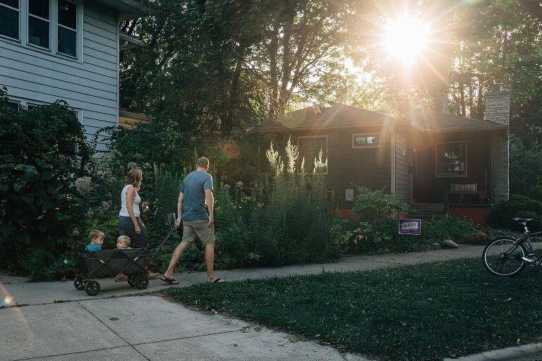 Family of four take walk and wagon ride in the neighborhood. Sunflare is present. 