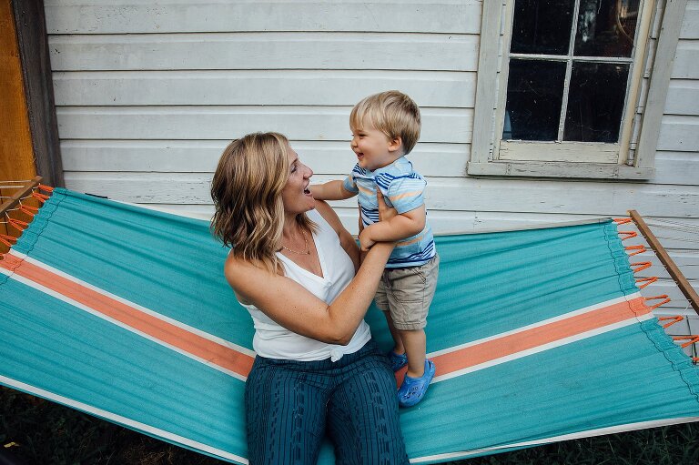 Mom and toddler son are smiling and playful with each other on colorful hammock in the backyard. Great for Backyard Family Photos