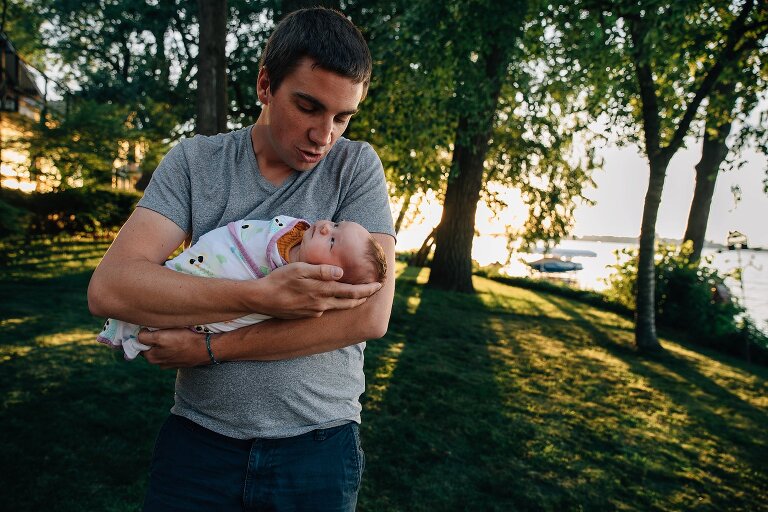 Newborn looks at Dad while being swaddled in the backyard on the lake 