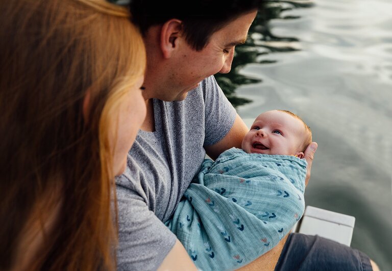Newborn smiles at parents in the backyard on the lake 
