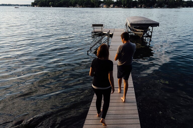Two people walk out onto their pier on the lake at sunset