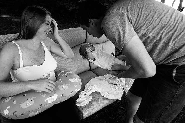 Dad holds crying newborn while mom prepares to nurse in the backyard swing