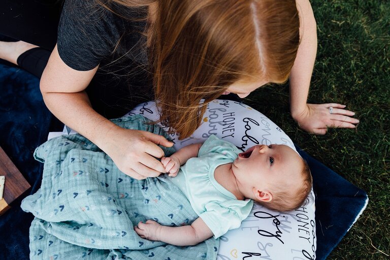 Newborn yawns from Boppy in the backyard while mom leans in over her.
